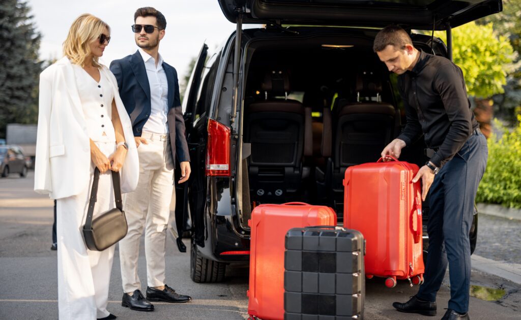 Two stylish travelers with luggage near a black van.