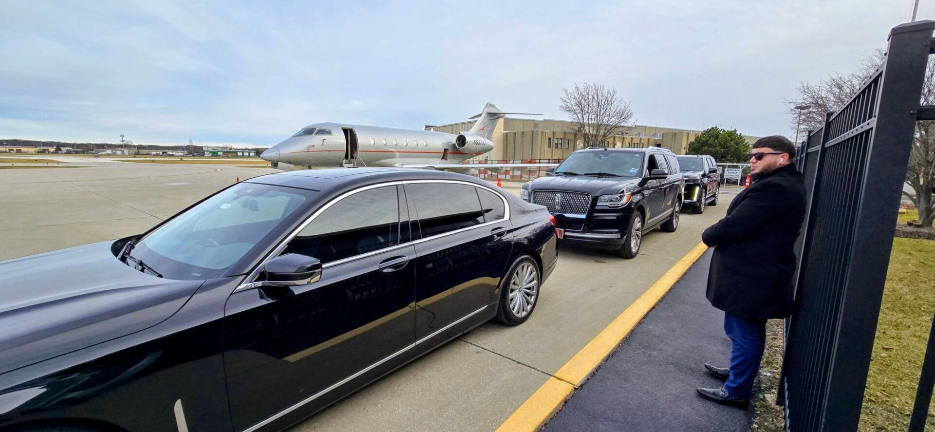 Two black luxury cars parked on a runway with a private jet in the background.