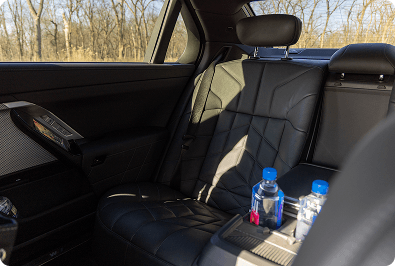 Sunlit car interior with black leather seats and water bottles.