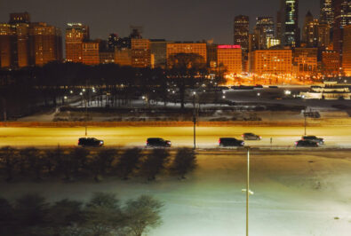 City skyline at night with illuminated buildings and foggy foreground.