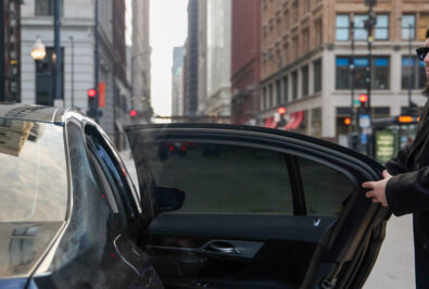 Open car door on busy city street with tall buildings and traffic lights.