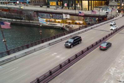 A black SUV driving on an urban bridge over a water canal.